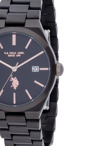 Orologio da polso analogico nero con cassa tonda, indici color oro rosa e display della data. Presenta un bracciale in metallo nero e il logo U.S. Polo Assn.