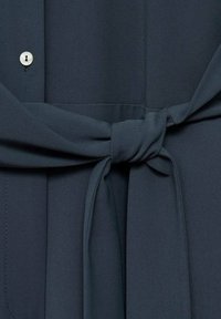 Tessuto grigio scuro con una texture liscia, dotato di una cintura annodata in vita e un dettaglio con bottone. Design semplice senza fantasie o accenti.