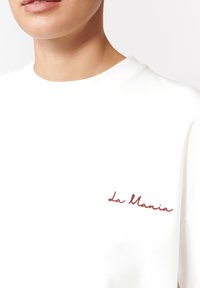 Biała bawełniana koszulka z okrągłym dekoltem i krótkimi rękawami, z czerwonym haftowanym napisem "la Mania" na lewej piersi.