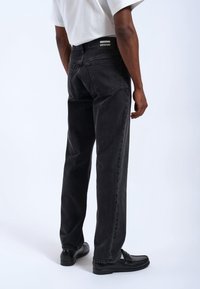 Jeans de mezclilla negra con un corte relajado, cuentan con pierna recta, diseño de cinco bolsillos y parche de marca cerca de la cinturilla.