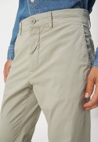 Pantaloni in cotone beige con una finitura liscia, dotati di chiusura con bottone, tasche anteriori e una vestibilità leggermente affusolata.