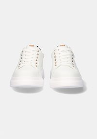 Zapatillas blancas hechas de material sintético suave con punta redonda, suela blanca gruesa y diseño de cordones con ojales dorados.