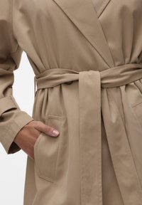Trench coat beige con cintura, dal finish testurizzato, caratterizzato da colletto a scialle, tasche laterali e tessuto arricciato in vita.