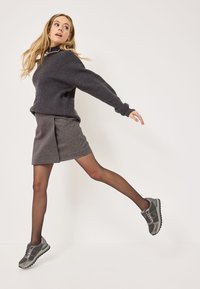 Grauer gerippter Pullover mit übergroßen Ärmeln, kombiniert mit einem dunkelgrauen A-Linien-Rock und grauen Sneakers, vor einem neutralen Hintergrund.