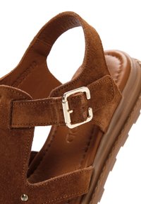 Sandal de ante marrón con diseño de espalda abierta, que cuenta con una hebilla metálica plateada, suela gruesa y parte superior texturizada para agarre y comodidad.