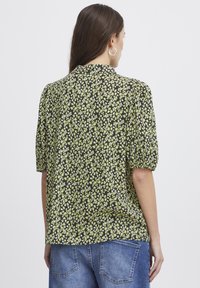 Blumenbluse in Schwarz mit kleinen grünen und weißen Blumen. Mit kurzen, puffartigen Ärmeln und Rundhalsausschnitt. Weicher, leichter Stoff.