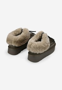 Par de zapatos de plataforma marrón oscuro con un grueso forro de piel de oveja beige alrededor del tobillo y detalle de cordones negros en la parte posterior.