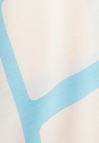 Textilie s jasně béžovým pozadím a výraznými, nepravidelnými modrými vzory. Hladká textura a jemný matný povrch.