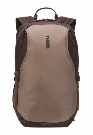Sac à dos Thule marron et beige avec poignée supérieure, bretelles rembourrées, compartiments avant zippés et sangles latérales réglables.