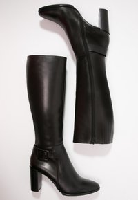 Pari nahan musta nahast kõrge säärega saapad plokk-kandadega, külgmise tõmbluku ja dekoratiivse pandlaga välimisel pahkluudel.