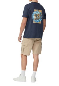 Marineblauwe katoenen t-shirt met grafisch ontwerp op de achterkant, gecombineerd met beige cargoshorts, witte sneakers en witte sokken.