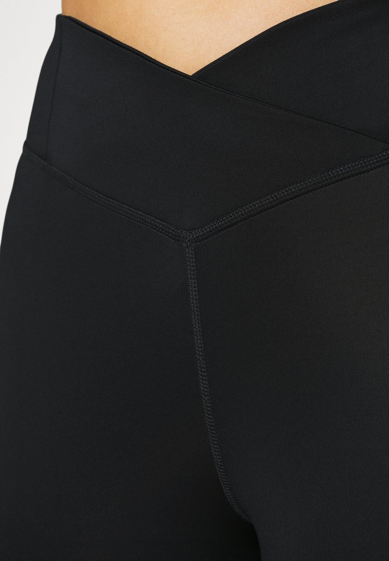 Leggings negros de cintura alta, confeccionados en una suave y elástica tela. Presentan un diseño de cintura cruzada y costuras planas visibles.