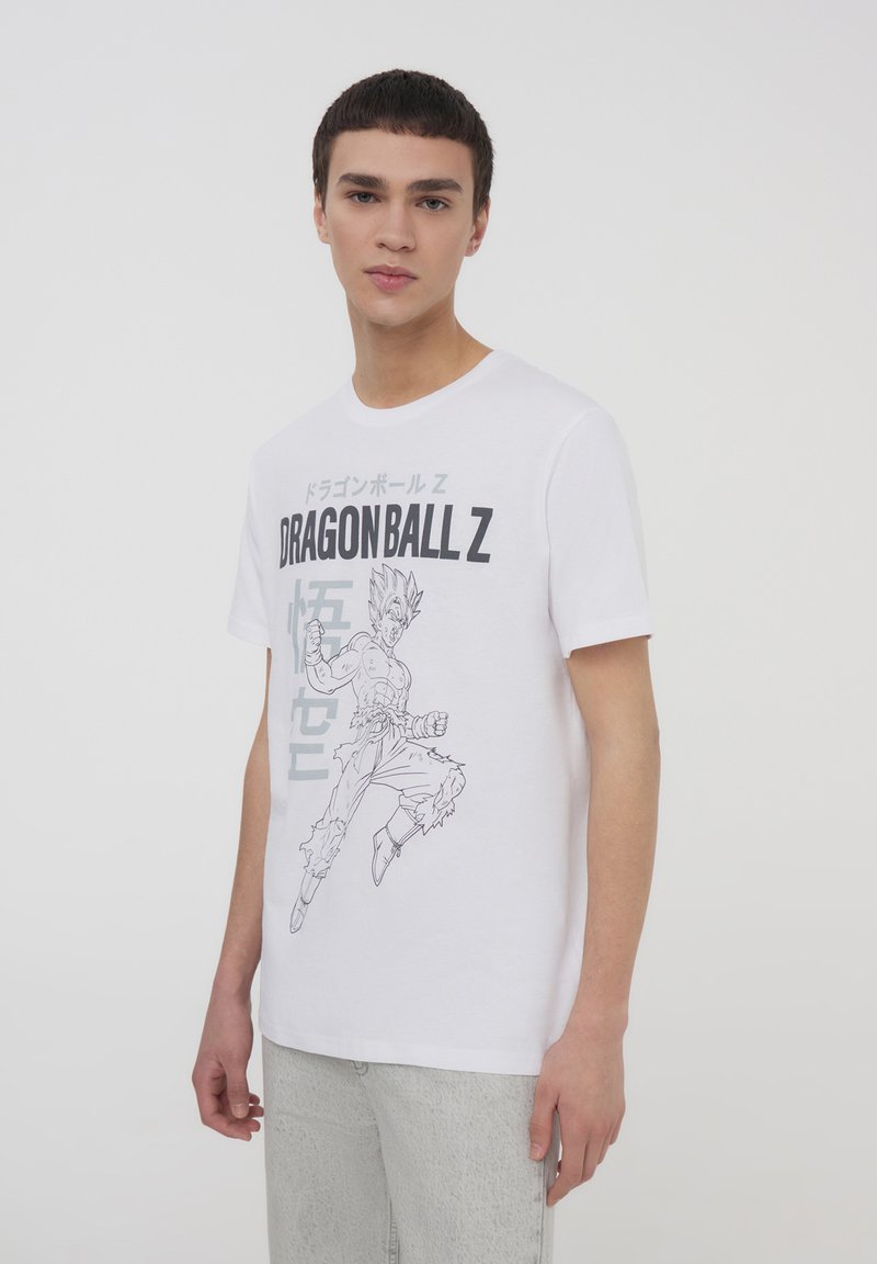 T-shirt bianco in cotone con stampa grafica di un personaggio di Dragon Ball Z, con testo e contorni grigi, maniche corte e scollo rotondo.