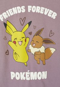 Lila T-Shirt mit Illustrationen von Pikachu und Eevee. Der Text lautet "FREUNDE FÜR IMMER" in fetten weißen Buchstaben, umgeben von kleinen Herzen.