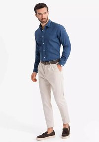 Camicia in denim blu scuro con bottoni, abbinata a pantaloni beige chiaro a sigaretta. Una cintura marrone e scarpe marroni scure completano l'outfit.