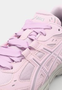 Gaiši rozā sporta kurpe ar teksturētu virsu, plāniem šņorēm un gumijas zoli, ar dekoratīvām izgriezumiem un pastiprinātu purngalu.