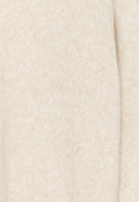 Tissu tricoté doux couleur crème avec une texture subtile, duveteuse et un motif de couture fin et régulier.