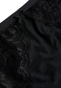 Zwarte kantdetails in combinatie met een zachte stof. Kenmerkt zich door ingewikkelde patronen en een zachte textuur, geaccentueerd met kleine stippen.