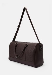 Brown duffel bag made of patterned synthetic material, featuring dual handles and an adjustable shoulder strap. Zip closure at top.