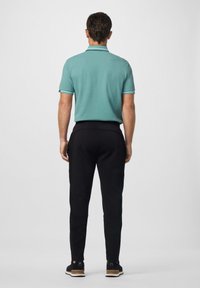 Polohemd in Aqua mit gestreiftem Kragen, kombiniert mit schwarzen, schmal geschnittenen Jogginghosen mit Seitentaschen und elastischen Bündchen, getragen mit schwarzen Schuhen.