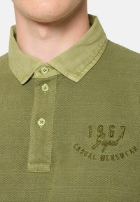 Tummanvihreä polo-paita, jossa on teksturoitu kangas, nappikaulus ja kolme nappia. Sisältää brodeeratun logon "1967" ja "Casual Menswear".