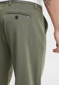 Olive green trousers with a smooth texture, featuring a back pocket with a black button and a subtle waistband design.