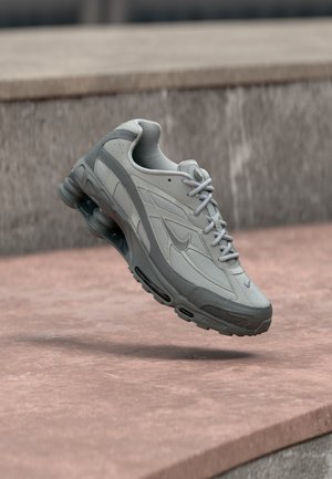 Szary i biały sneaker Nike zawieszony nad kamiennym stopniem z widocznym poduszkowym systemem powietrznym i teksturowaną podeszwą.