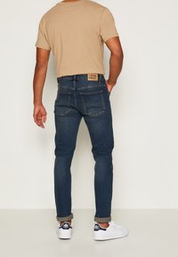 Blå denimjeans med slim fit, med fem fickor, uppvikta ärmslut och en beige etikett på baksidan av midjan. I kombination med vita sneakers.