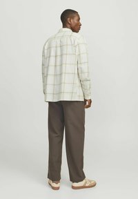 Camisa de cuadros beige con cuello, corte relajado, mangas largas, combinada con pantalones oscuros marrones y zapatillas beige con detalles.