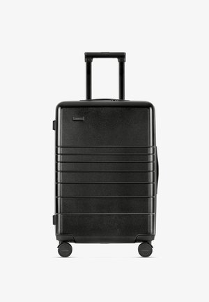 Valise rigide noire avec une poignée télescopique, quatre roues et des rainures horizontales sur la surface avant pour plus de texture.