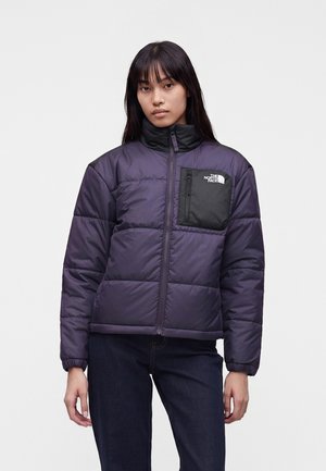 Ung kvinde med glat mørkt hår har en lilla dunjakke på med en sort brystlomme og The North Face-logo.
