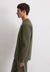 Sweatshirt vert olive en coton doux, avec un col rond, des manches longues et des poignets en côtes. Design simpliste avec des coutures minimales.