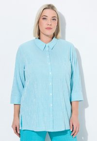 Camicia azzurro chiaro, con bottoni, a righe verticali, colletto e maniche a tre quarti. Presenta una vestibilità comoda e spacchi laterali per maggiore facilità.