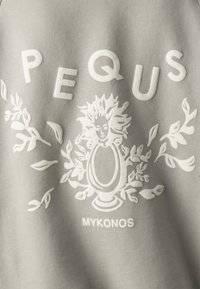 Siva tkanina z belim reliefnim napisom "PEQUS" in dekorativnim emblemom, ki prikazuje obraz obdan z listi. Spodaj je napis "MYKONOS."