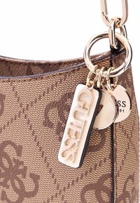Borsa tote marrone con motivo, realizzata in un tessuto testurizzato, dotata di dettagli in oro, accenti a forma di chiave circolare e un prominente etichetta con il logo GUESS.