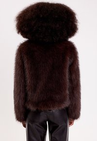 Manteau en fourrure marron avec une texture douce et dense, design court et manches longues. Associé à un pantalon en cuir noir, vu de l'arrière.