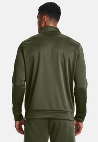 Dunkelolivgrüne Trainingsjacke mit glatter Textur, Stehkragen und langenÄrmeln. Sie hat ein tailliertes Design und Rippdetails am Saum.