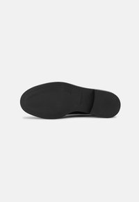 Black shoe sole with smooth rubber surface and textured lines, featuring a rounded toe and subtle branding. Flat design for stability.