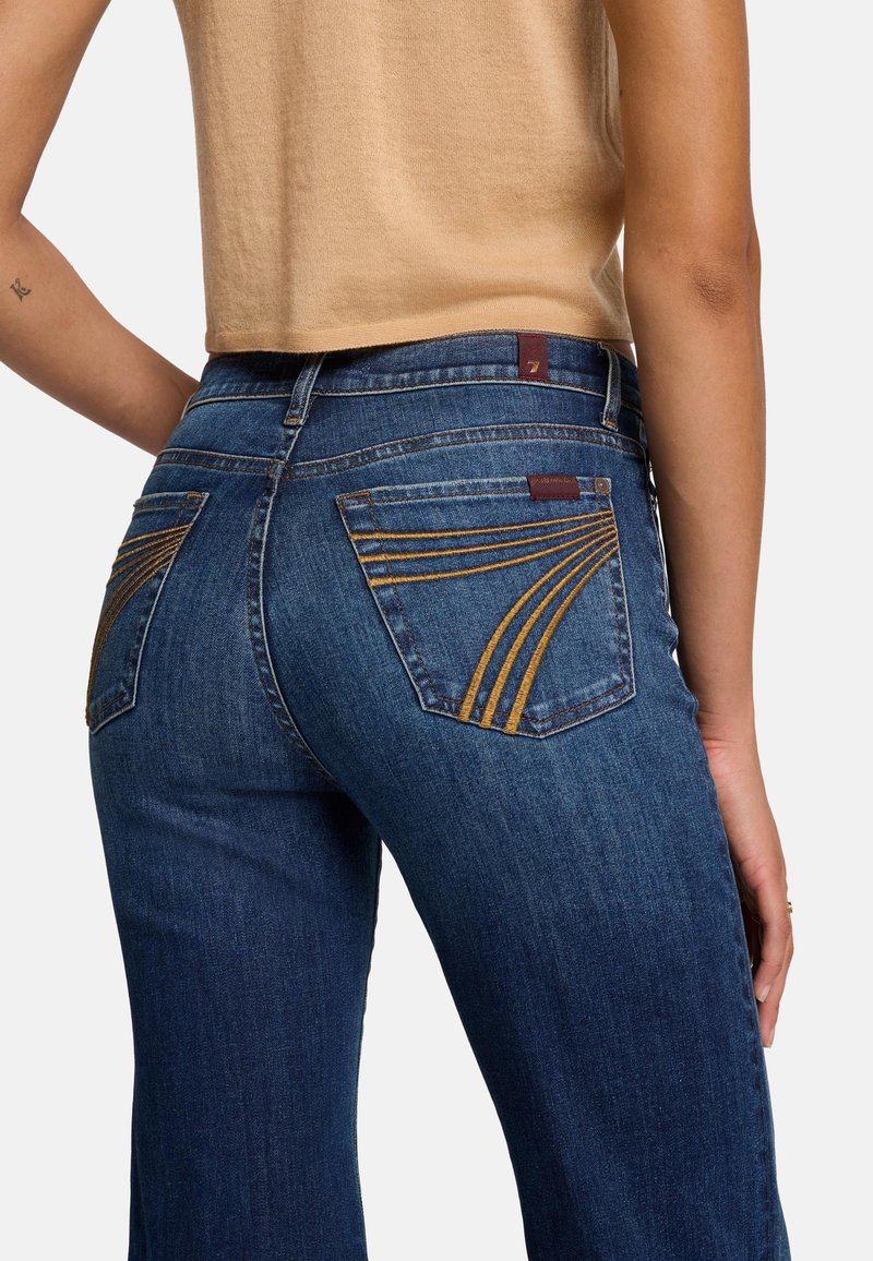 Denim jeans in dark blue, featuring a straight leg cut, contrasting mustard yellow stitching on back pockets, and a leather brand tag.