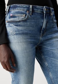 Hellblaue Jeans aus Denim mit leichter Auswaschung, ausgestattet mit einem bestickten Blumenmuster am Oberschenkel, sichtbaren Nähten und einem Fünf-Taschen-Design.