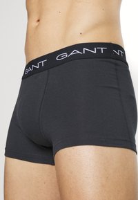 Schwarze Boxershorts aus glattem Stoff, mit einem breiten schwarzen Bund und weißem "GANT"-Logo sowie einer engen Passform.