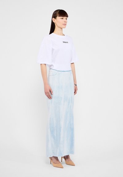Hvit avkortet t-skjorte med svart tekst, kombinert med en lys blå, tie-dye, denim maxiskjørt. Modellen bruker nude spissede hæler.