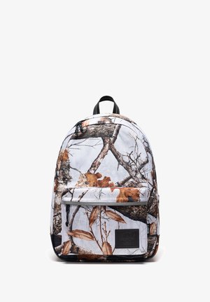 Sac à dos avec un fond blanc et un motif camouflage de feuilles d'automne marron et grises ainsi que des branches d'arbre, poche avant zippée et anse noire.