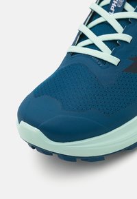 Basket de course avec une tige en nuphar sombre texturée, une semelle en caoutchouc bleu clair et des lacets bleu clair. Présente un design moderne et épuré avec des textures superposées.