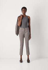 Graues Tanktop, gemusterte Hose in Creme und Schwarz, strukturierte Jacke über dem Arm drapiert und flache schwarze Schuhe. Einfaches Design mit taillierter Passform.