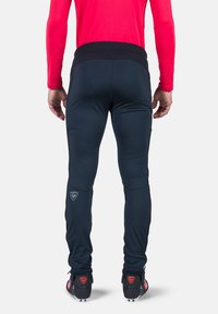 Marineblaue Sporthose mit einem kontrastierenden schwarzen Bund, ausgestattet mit schmal zulaufenden Beinen, Seitennähten und einem Logopatch am unteren Bein.