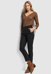 Haut à imprimé léopard marron avec un col en V, manches 3/4 ; pantalons noir à rayures taille haute ; bottes à talon carré en suède marron.