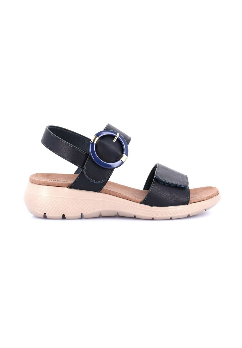 Sandal in pelle nera con cinturino alla caviglia regolabile e grande accentuazione circolare. Soletta imbottita su una suola leggera e texturizzata di colore crema.