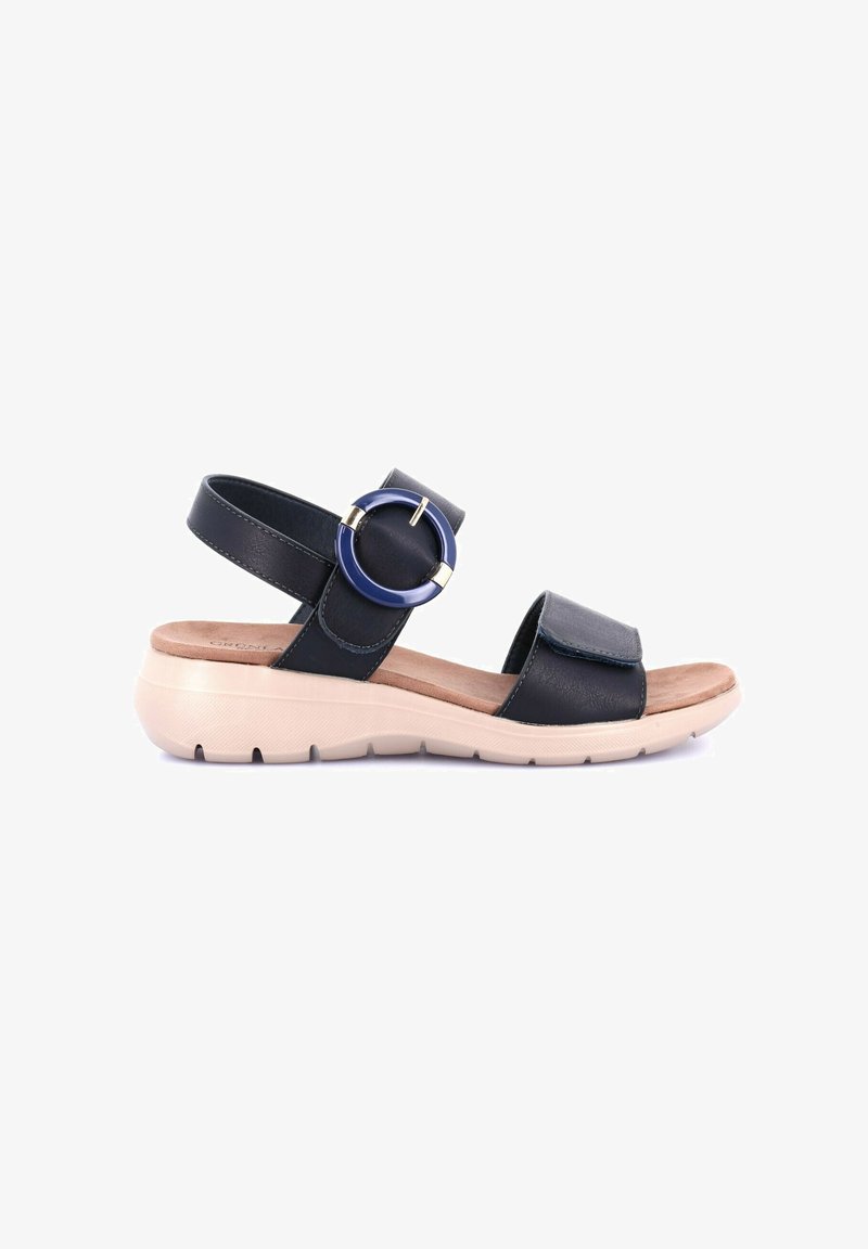 Sandal in pelle nera con cinturino alla caviglia regolabile e grande accentuazione circolare. Soletta imbottita su una suola leggera e texturizzata di colore crema.