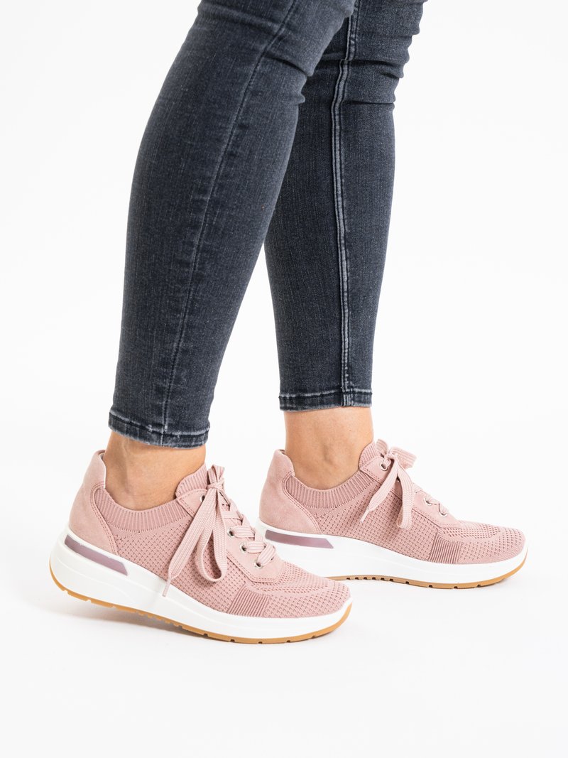 Person wearing black skinny jeans and pink knit lace-up sneakers with white soles, standing on a white background.